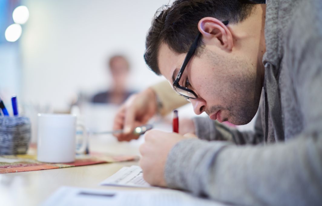 Ein junger Mann sitzt über den Tisch gebeugt und füllt ein Formular aus.