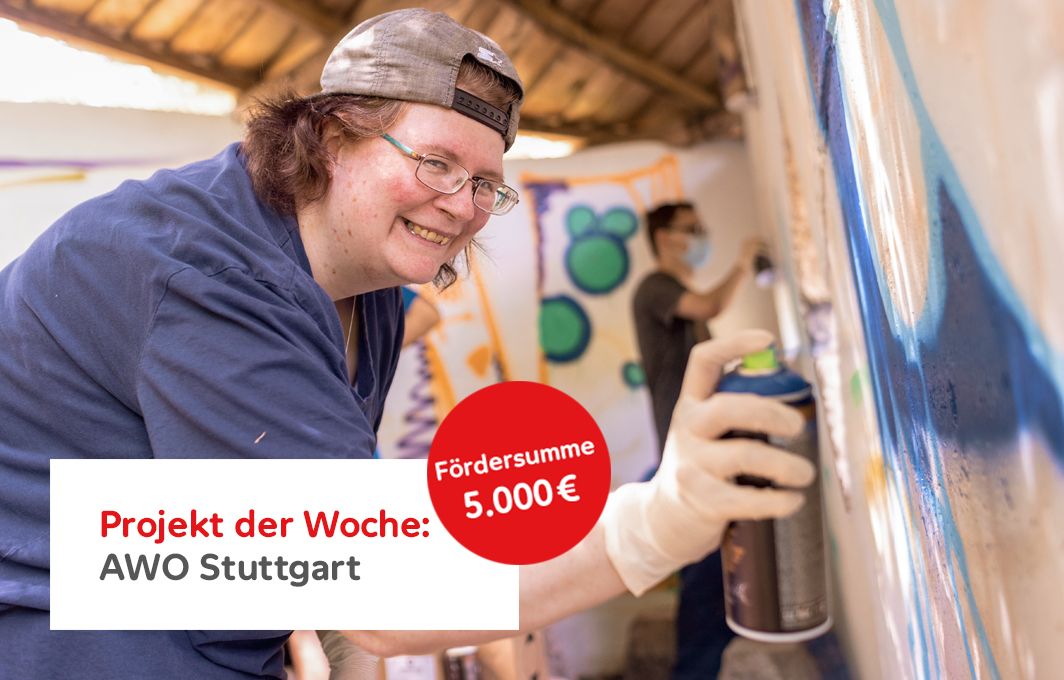 Eine Frau mit Kappe sprüht etwas mit einer Spraydose an eine Mauer. Sie lacht in die Kamera.