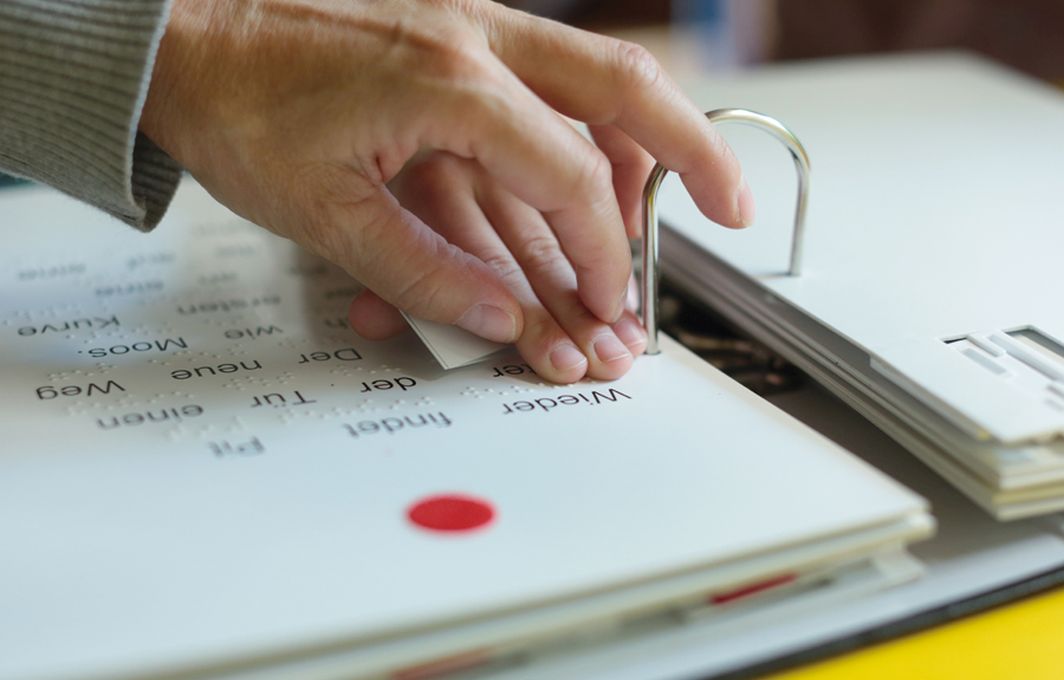 Zwei Hände erfühlen einen Text in Brailleschrift.