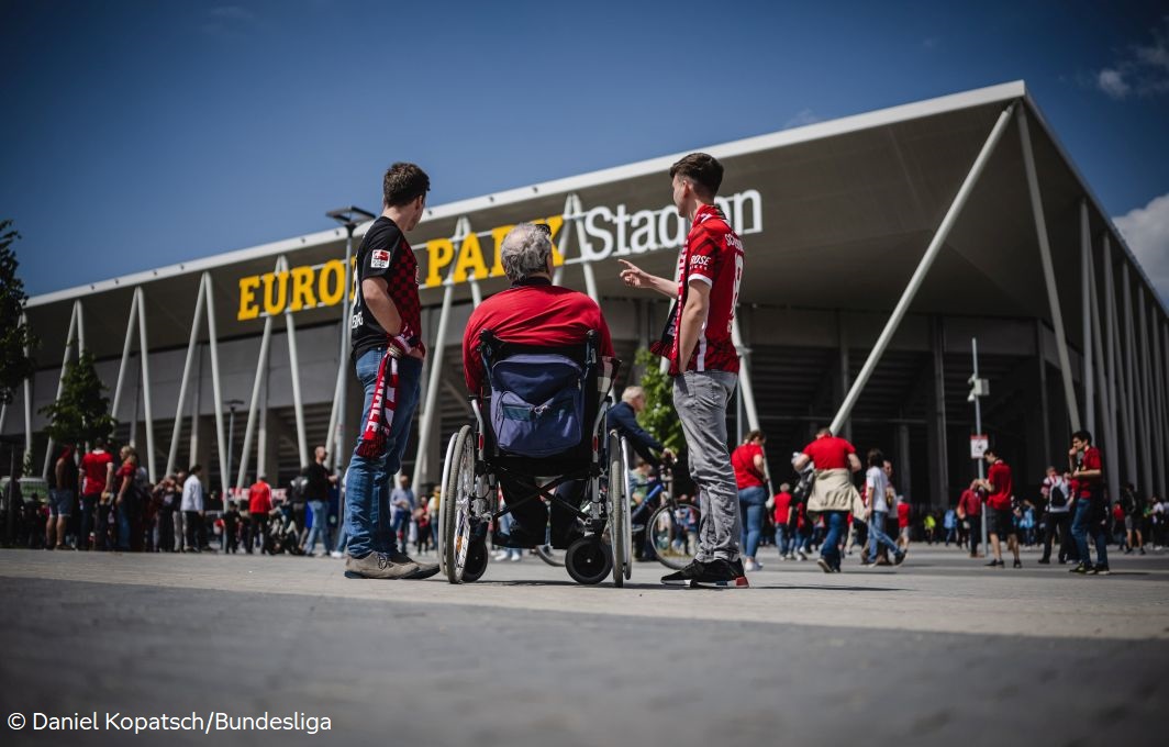 Zwei Menschen, einer davon im Rollstuhl, stehen vor dem Europa-Stadion in Freiburg.