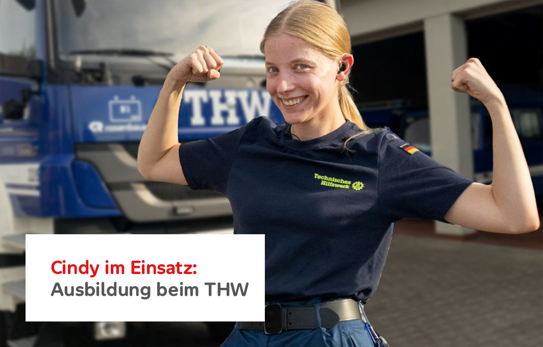 Cindy steht vor einem Fahrzeug des THW. Die Arme hat sie angewinkelt und zeigt Stärke.