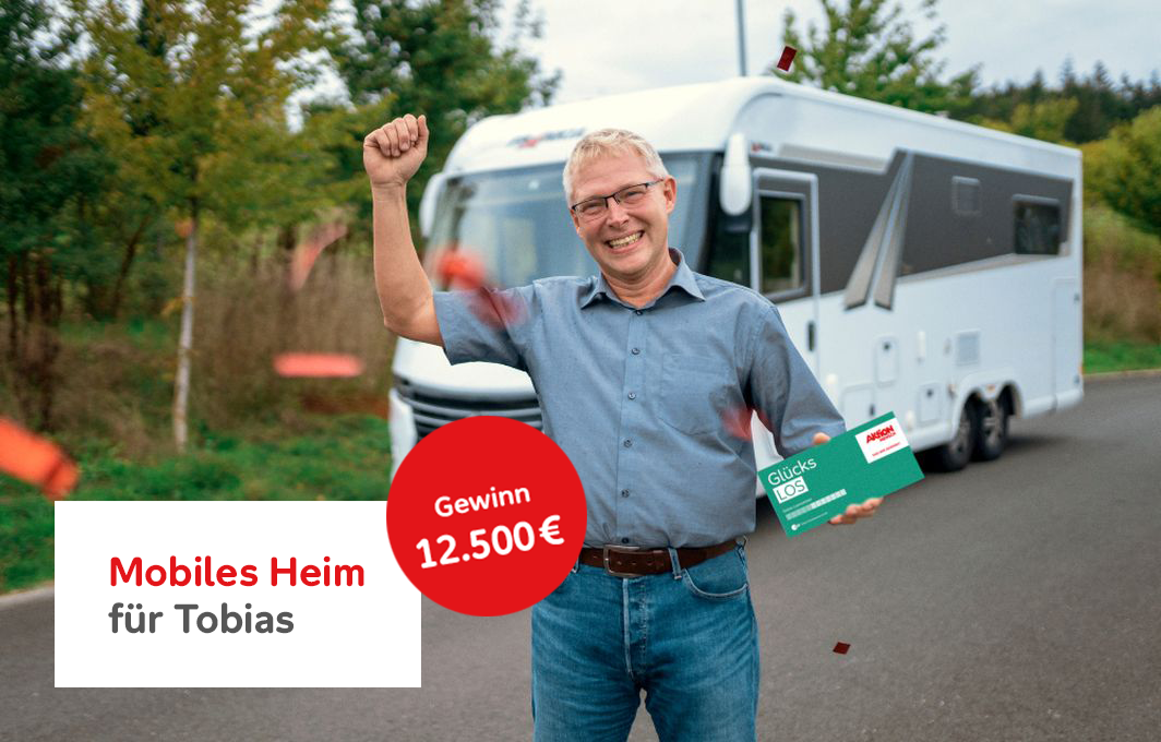 Gewinner Tobias steht vor seinem Wohnmobil. Mit der linken Hand hält er das Glücks-Los, mit dem rechten Arm jubelt er.