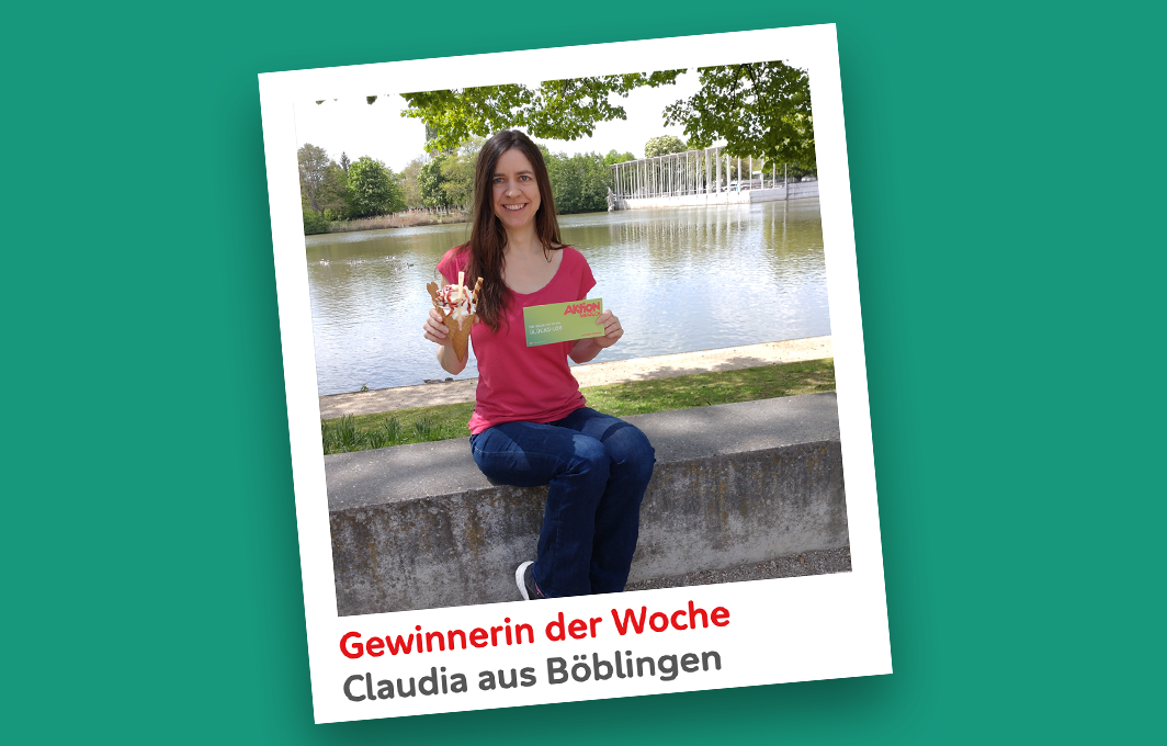 Die Gewinnerin Claudia sitzt auf einer Mauer vor einem See und hält ihr Los und ein Eis in den Händen.