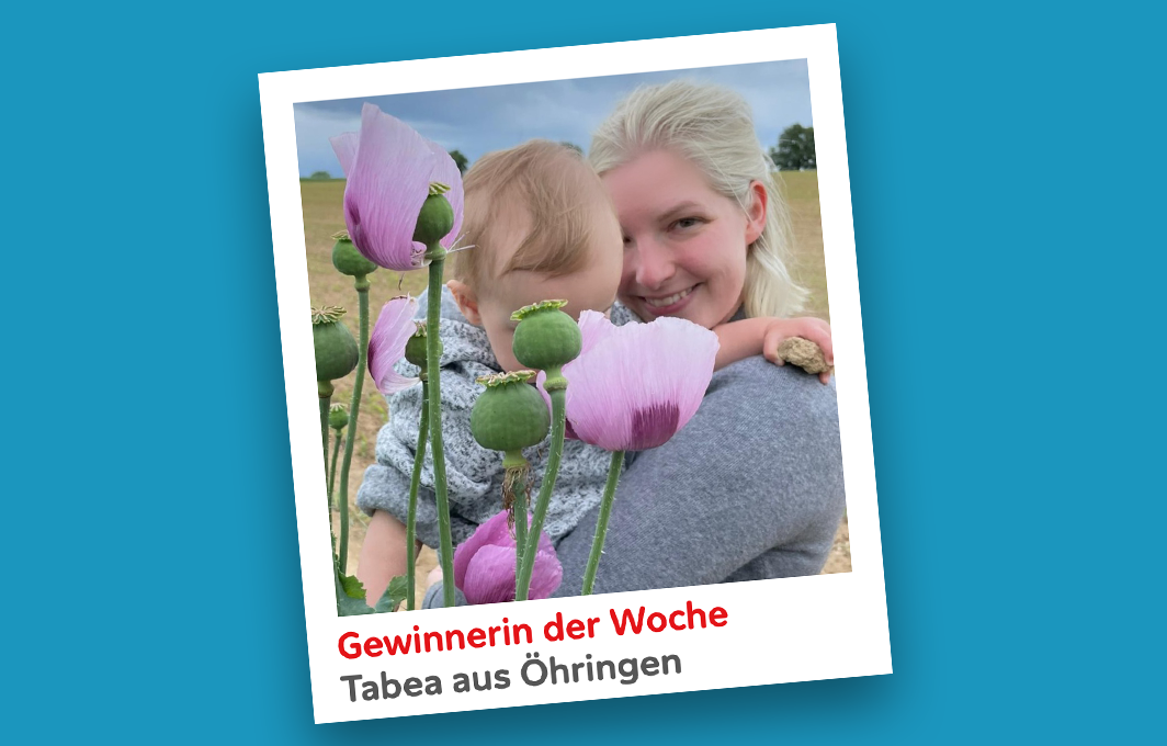 Gewinnerin Tabea hält ihr Kind im Arm und lacht in die Kamera. Im Vordergrund verdecken Blumen das Gesicht des Babys.