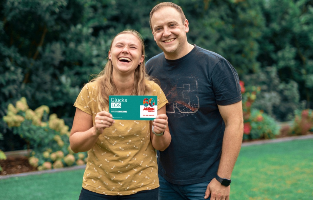 Ein Pärchen hält lachend ein Glücks-Los in der Hand.