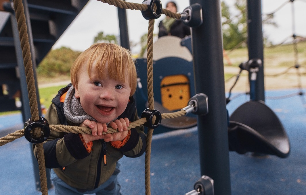 Ein Junge mit Down-Syndrom spielt auf einem inklusiven Spielplatz.