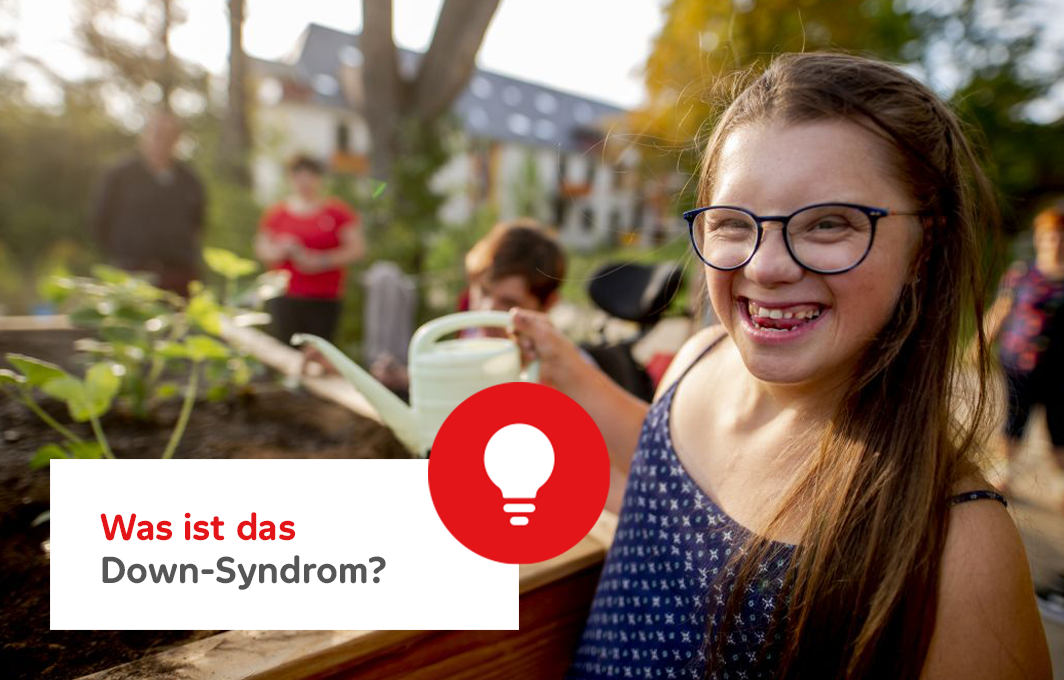 Ein Mädchen mit Down-Syndrom grinst in die Kamera, während es Blumen in einem Hochbeet gießt. Infokasten: Was ist das Down-Syndrom?