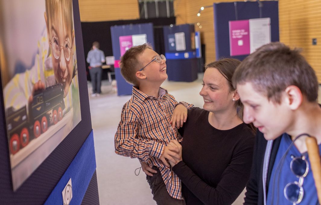 Eine Frau und zwei Jungen mit Sehbehinderungen schauen sich eine Infotafel im Museum an.