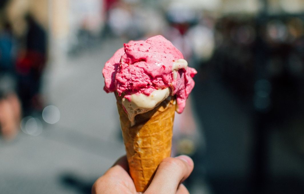 Eine Hand hält eine Waffel mit zwei Kugeln Eis in die Höhe.