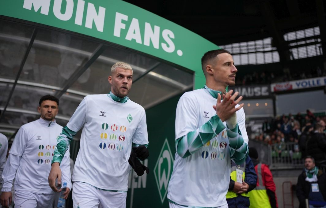 Drei Spieler des SV Werder Bremen beim Einlauf ins Weserstadion. Über ihnen sieht man den Schriftzug "Moin Fans"