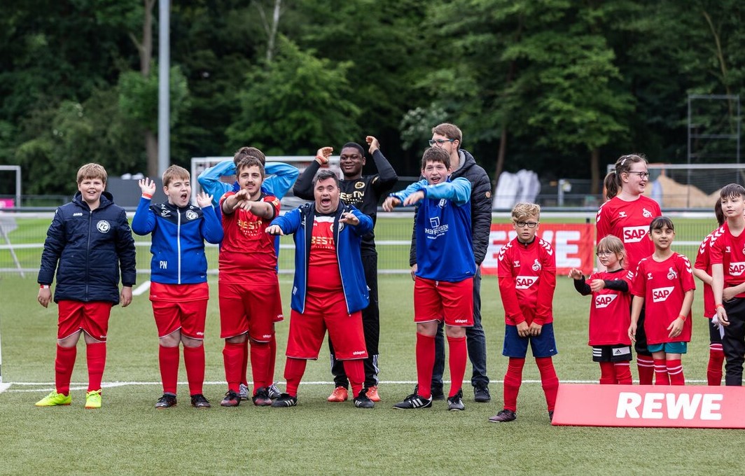 Eine inklusive Jugend-Fußballmannschaft steht jubelnd auf dem Platz.