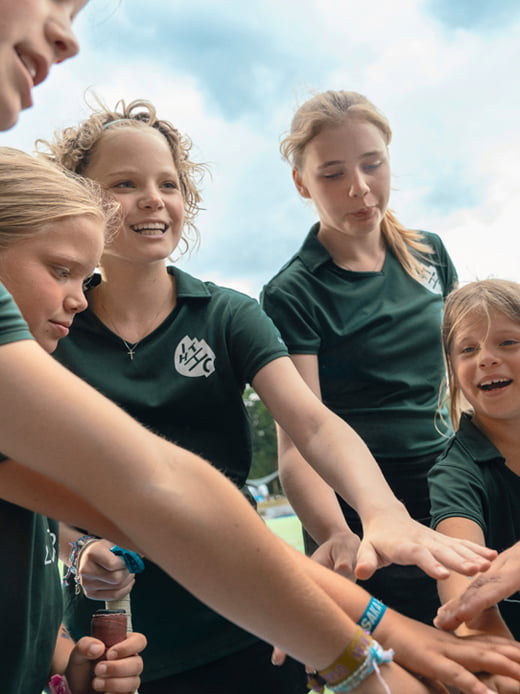 Die jugendlichen Spielerinnen einer inklusiven Hockey-Mannschaft stehen im Kreis auf einem Sportplatz. Sie haben ihre Hände in die Mitte gestreckt und lachen fröhlich.