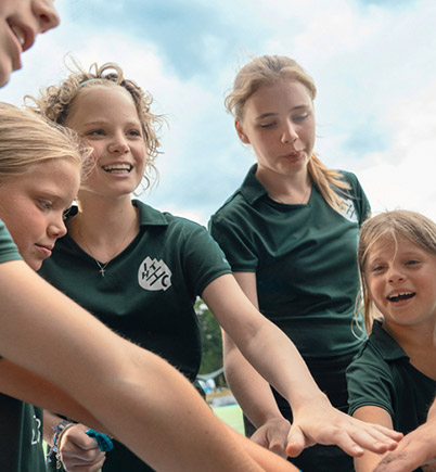 Die jugendlichen Spielerinnen einer inklusiven Hockey-Mannschaft stehen im Kreis auf einem Sportplatz. Sie haben ihre Hände in die Mitte gestreckt und lachen fröhlich.